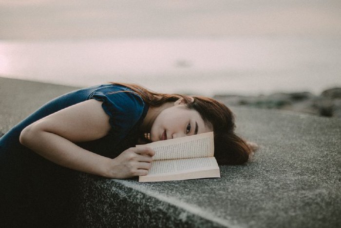 Жена чете книга на плажа по залез